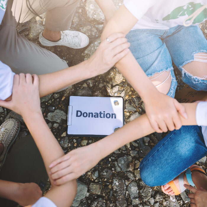 Four hands joined together over a donation sign