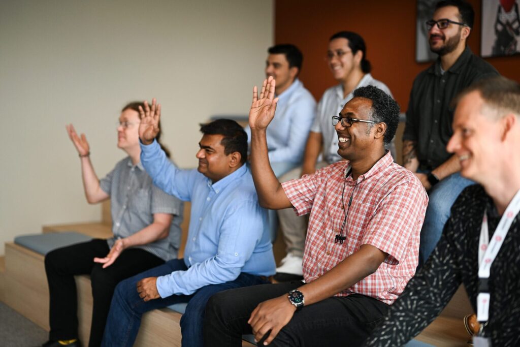 Creative Tech sitting together and smiling with four people in the group raising their hands