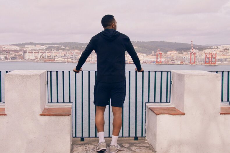 A man on a ledge admires the stunning ocean view, surrounded by the beauty of nature and the sound of waves.