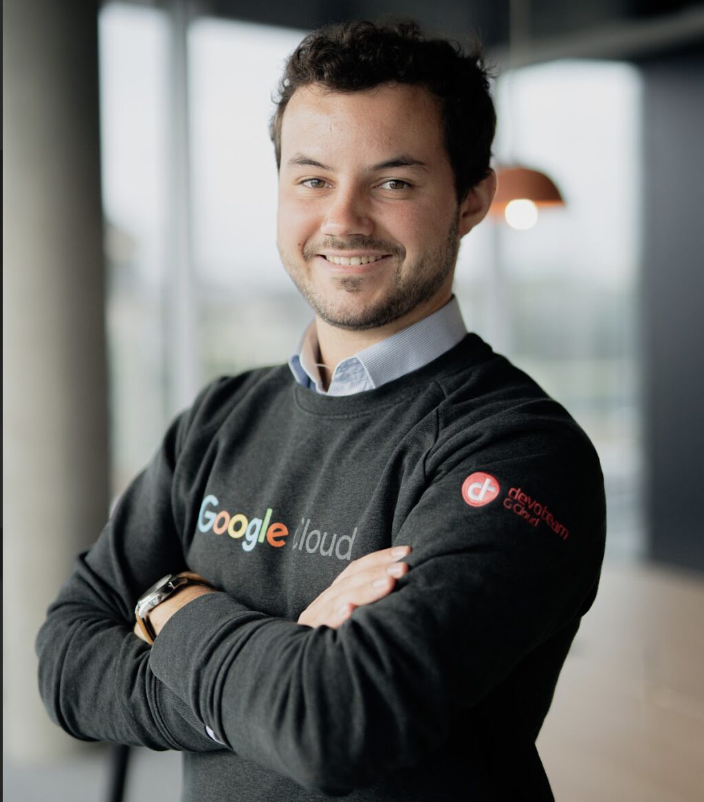 A portrait of Harold Snyers - ML & Data Engineer standing in an office, wearing a sweatshirt with Google and Devoteam logos