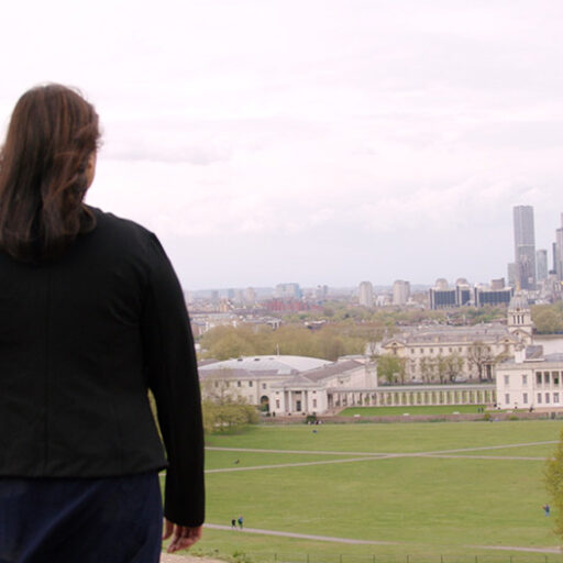 A person from the back standing o a hill and watching a landscape